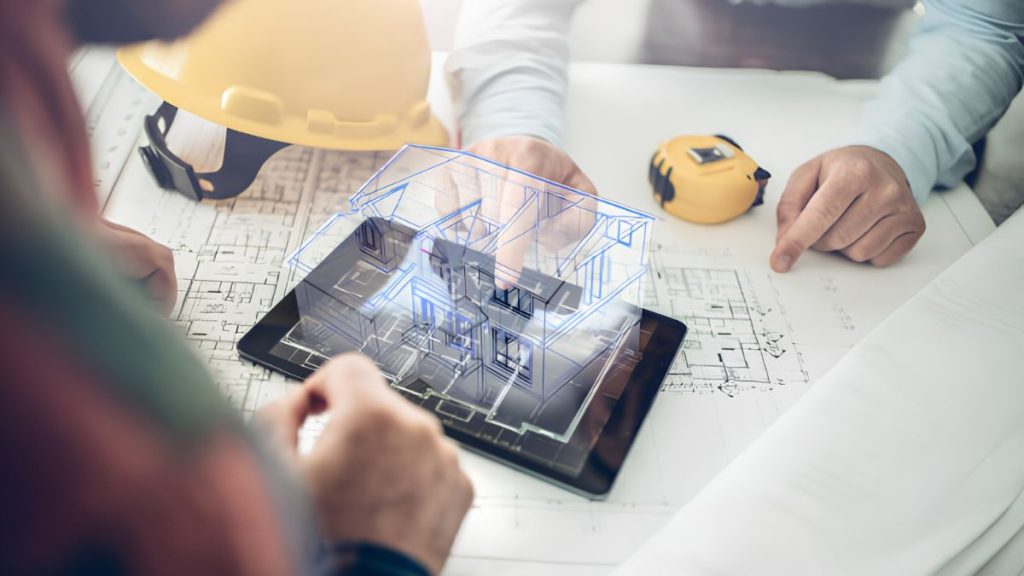 Architects review a 3D house model projected on a tablet over blueprint plans and construction tools nearby.