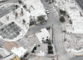 Aerial view of a construction crew on a partially demolished rooftop, wearing hard hats and safety gear around exposed steel framework.