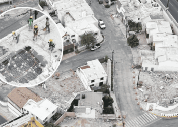 Aerial view of a construction crew on a partially demolished rooftop, wearing hard hats and safety gear around exposed steel framework.