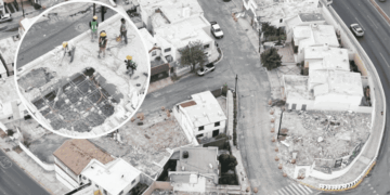 Aerial view of a construction crew on a partially demolished rooftop, wearing hard hats and safety gear around exposed steel framework.