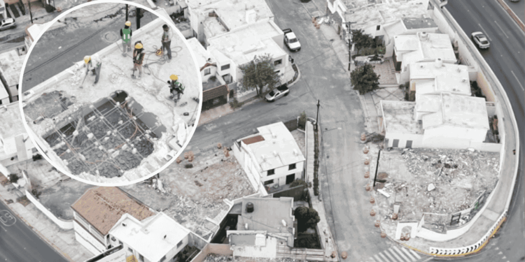 Aerial view of a construction crew on a partially demolished rooftop, wearing hard hats and safety gear around exposed steel framework.