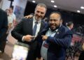 adrian-de-la-garza-monterrey - LA VISION 360 Two suited men smiling and posing together at an event, one with his arm around the other’s shoulder while they point at each other in agreement.