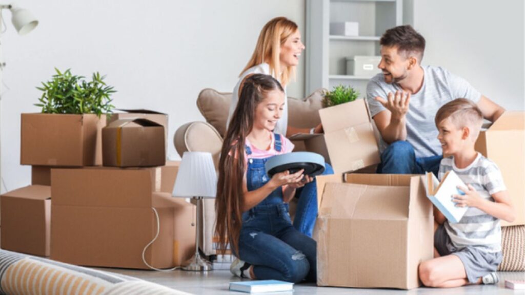 vision-360-calculadora-de-escrituras-nuevo-leonjpg - LA VISION 360 Family of four unpacking boxes in a bright living room, smiling and talking during a move.